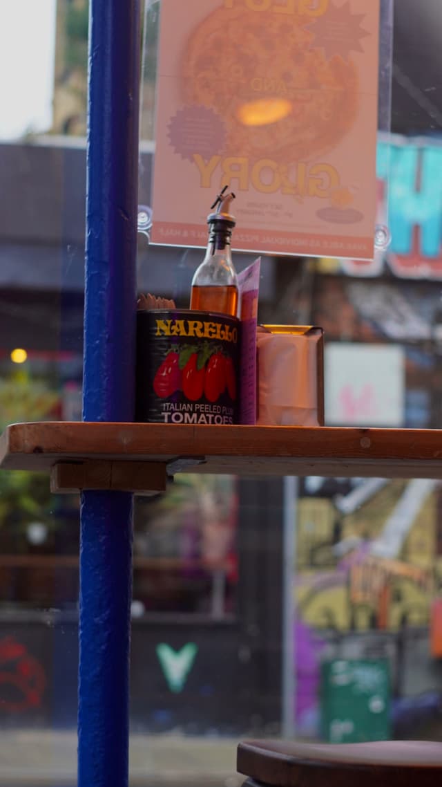 A can of Pizza sauce stands on a wooden table by a window, with colorful street art visible in the blurred background